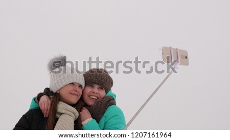 Mom with daughter, photograph selfie on phone, winter snow park. They laugh, smile and take pictures.