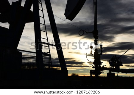 A silhouette image of a working pump jack at sunset. 
