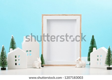 Little toy white houses, white rabbits and christmas decoration. Empty frame with the copy space for text over blue pastel background. Christmas celebration idea