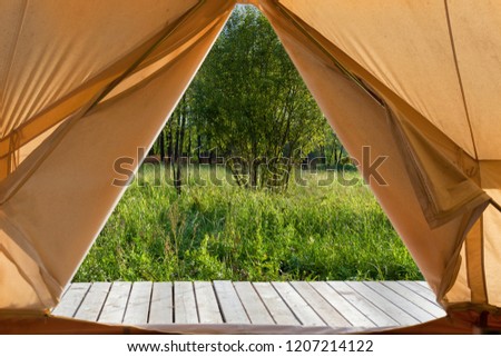 View from the canvas tent upon the green meadow with trees. POV Royalty-Free Stock Photo #1207214122