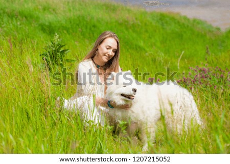 young woman sitting with a big white shaggy dog on a background of the river in the green grass