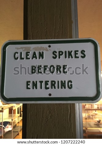 Sign on pole at golf course that reads:  Clean Spikes Before Entering