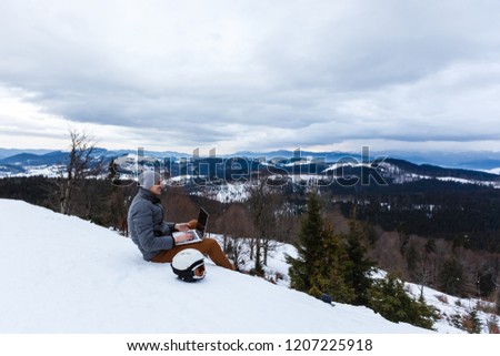 A young man with a laptop sitting at cliff edge on mountain top