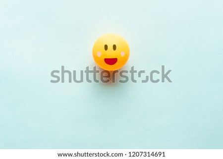 Happy smiling yellow face illustration on a ping pong ball on blue background with negative space for text