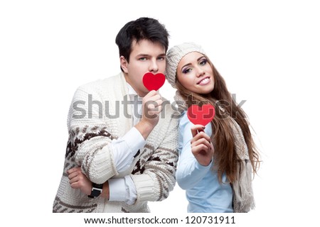 young casual caucasian brunette couple in winter clothing cover their mouths with red hearts and looking at camera with wide opened eyes