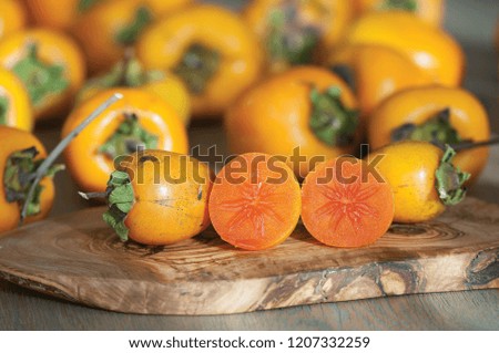 the ripe persimmon and its cutted pieces on a wooden table over the background with persimmon fruits