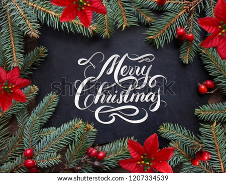 Merry Christmas hand lettering inscription with golden balls, tree branches and cones on a wooden background. Christmas greeting card. 