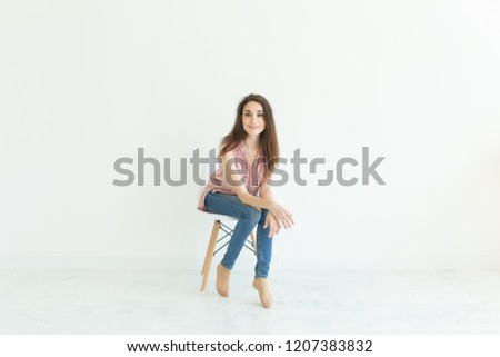people, beauty and fashion concept - young brunette woman posing on chair isolated on white background with copy space