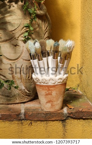 brushes stand in a ceramic pot, yellow background