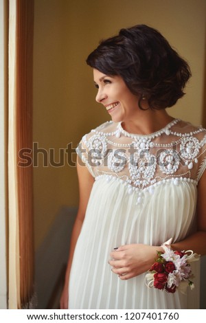 beautiful brunette woman in a white dress posing near the window.