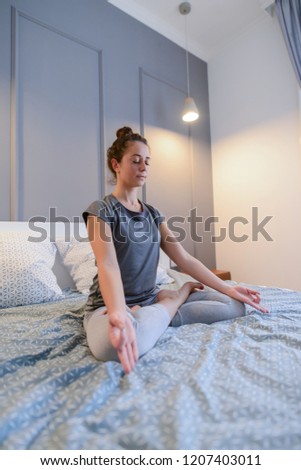 Picture of fit beautiful middle age woman sitting on her bed in lotus position.