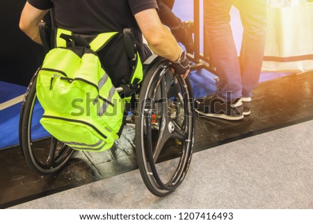 A wheelchair user visits an exhibition in a public place. Disabled person with protective green backpack