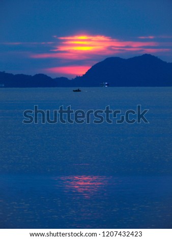 A cloudy, blue-tinged sunset near Koh Chang, Thailand. The sun sets leaving a small glow of light on the ocean.