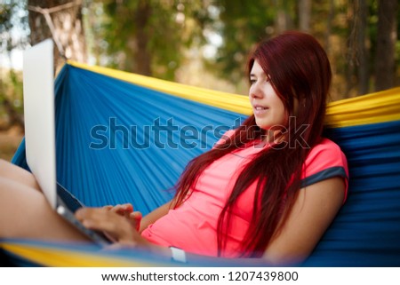 Photo on side of happy girl with laptop sitting in blue hammock