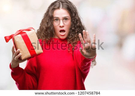 Young brunette girl holding a gift over isolated background with open hand doing stop sign with serious and confident expression, defense gesture
