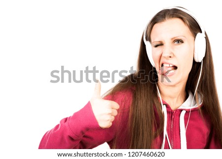 Young attractive smiling girl with long hair and pierced tongue listening the music by headphones and making faces. Advertising concept. Isolated on abstract blurred white background with copy space