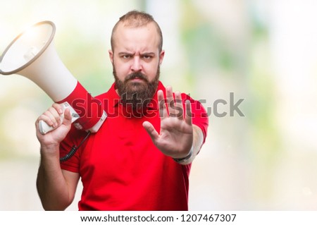 Young caucasian man shouting through megaphone over isolated background with open hand doing stop sign with serious and confident expression, defense gesture