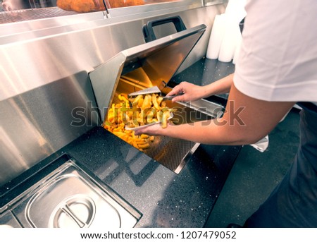 Cooking and serving delicious hot chips or French fries in a traditional British fish and chip shop. Royalty-Free Stock Photo #1207479052