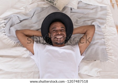 Young African American man in a hat lying on the bed.