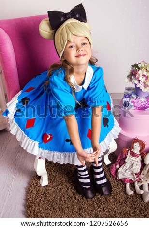 little girl in blue dress. kid christmas halloween costume. young happy girl in white room is sitting in pink armchair and flirting with beauty smile near gifts and hands down