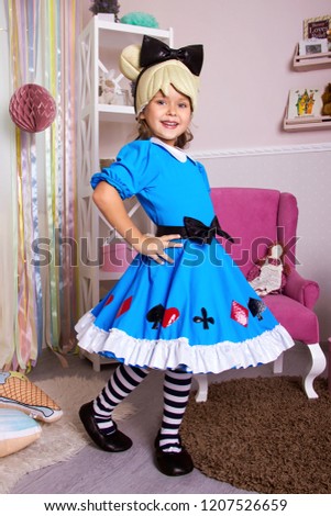 little girl in blue dress. kid christmas  halloween costume. young happy girl in white room is standing in pink armchair and flirting with beauty smile near gifts