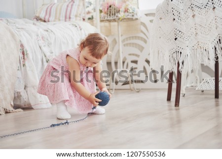 Childhood concept. Baby girl in cute dress play with colored thread. White vintage childroom.