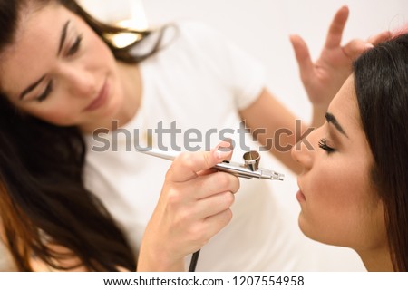 Make-up artist using aerograph making an airbrush make up to an African young woman in a beauty center. Beauty and Aesthetic concepts. Royalty-Free Stock Photo #1207554958