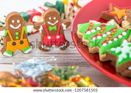 Tasty and cute baked Christmas cookies (gingerbread) with beautiful xmas decoration in red plate on light wooden table background, close up, copy space (text space)