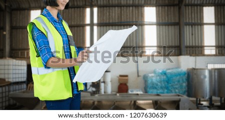 Female architect looking at blueprint against grey background against yellow crate by conveyor belt