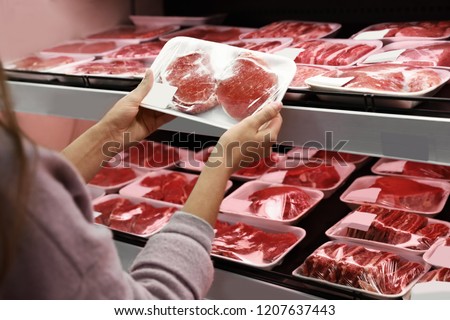 Woman taking packed pork meat from shelf in supermarket Royalty-Free Stock Photo #1207637443