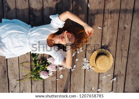 Attractive young hipster woman in white dress and straw hat lies on the wooden floor.