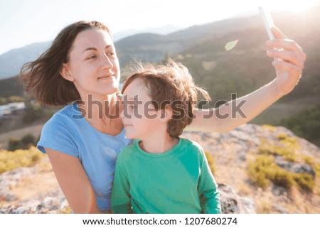 A woman with a boy on top of a mountain. Mom and her son make selfie on the background of a beautiful landscape. Traveling with a child.