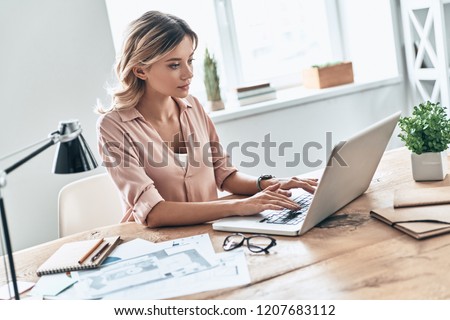 Her job is her hobby. Beautiful young woman in smart casual wear using laptop while sitting in modern office 