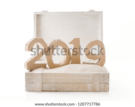 2019, handmade 3D numbers made of reused cardboard paper, in wooden chest with sand and on white background.