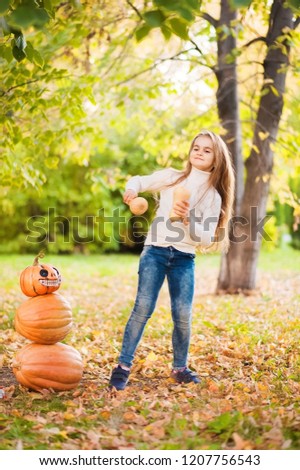 Little girl in a white sweater and jeans on a background of green textural natural background. A girl dancing with pumpkins near the pumpkin pyramid. Halloween concept