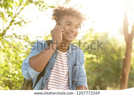 Image of handsome emotional young african guy in park outdoors talking by mobile phone.