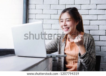 Blurred image of Happy excited Young Woman celebrate in cheerful posture when see a good news in Computer Laptop. Sitting nearby Window in House. Successful and Achievement Concept