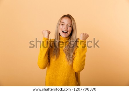 Portrait of a cheerful young woman dressed in sweater standing isolated over yellow background, celebrating success