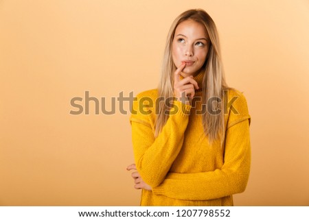 Portrait of a thoughtful young woman dressed in sweater standing isolated over yellow background, looking away