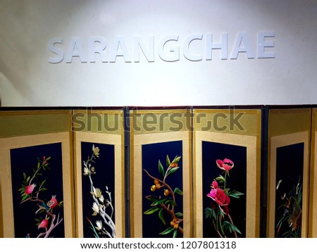 Folding construction with traditional Korean floral embroidery - down, and White Korean word WELCOME on the white wall - up