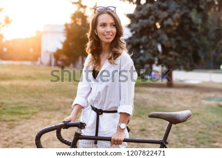 Smiling young woman spending time at the park, walking with bicycle