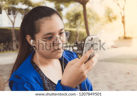 Beautiful asian gril use smartphone and listening to music in earphones at garden