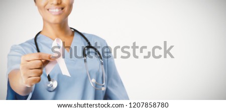 Smiling nurse holding breast cancer awareness pink ribbon between her fingers on a white foreground