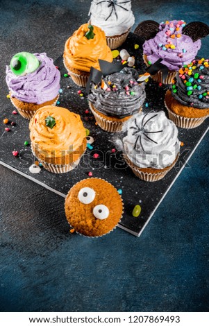 Funny children's treats for Halloween: variations of cupcakes, decorated in the form of different monsters, witches, pumpkins, ghosts. Dark rusty blue background copy space for text, top view