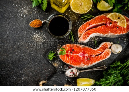 Raw salmon fish steaks with lemon, herbs, olive oil, ready for grill, slate cutting board, dark rusty background copy space