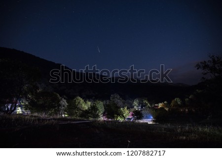 Beautiful night landscape with starry night mountains and forest. Night forest with green meadow and mountains in bright starry night or view of milky way