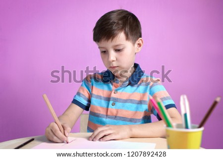 European boy carefully drawing with colorful pencils at home.
