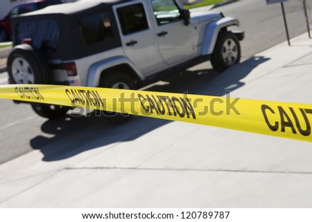 Close up of yellow caution tape with car in the background
