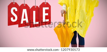 Woman in yellow raincoat holding an umbrella against pink background 