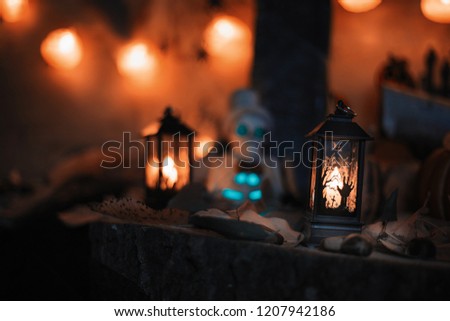 Halloween decorations concept at night. Close up of jack o'lantern, vintage lanterns, pumpkins, skull, autumn leaves. Colorful halloween lights on evening. Happy Halloween scene on wooden background
